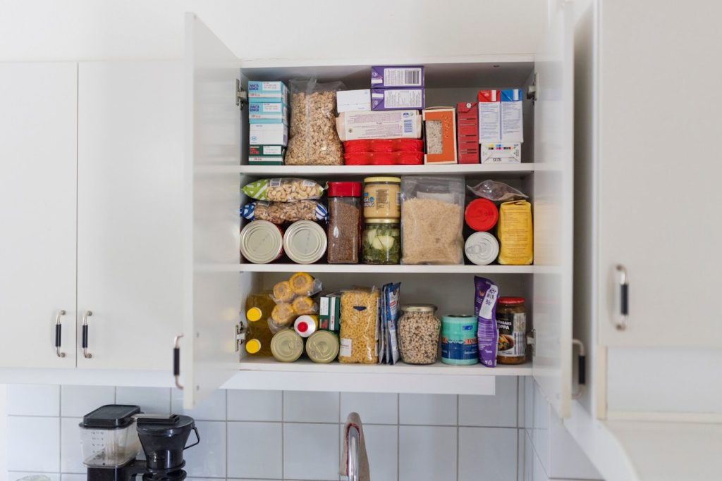 Ett köksskåp med hyllor fyllda med konserver, burkar, lådor och olika skafferivaror.