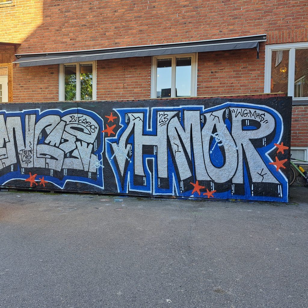 Graffitimålning med djärva bokstäver i silver och blått på en tegelvägg, dekorerad med röda stjärnor.