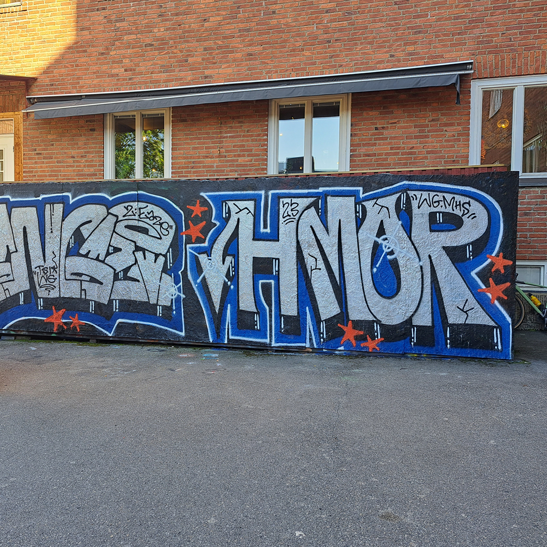 Graffitimålning med djärva bokstäver i silver och blått på en tegelvägg, dekorerad med röda stjärnor.
