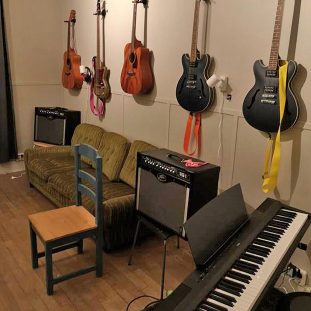 Musikrum med gitarrer på väggen, ett keyboard, förstärkare, en grön soffa och en trästol.