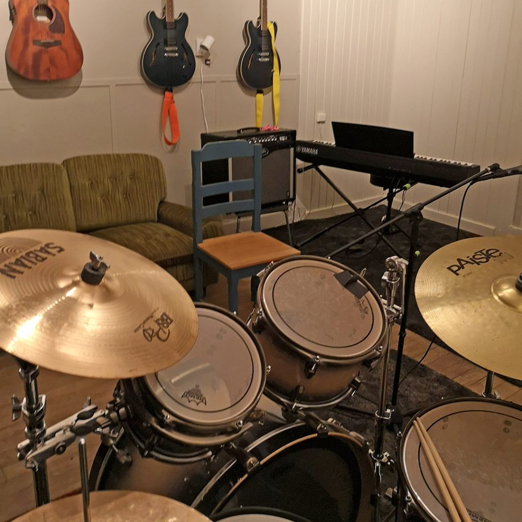 Ett musikrum med trumset, keyboard, gitarrer på väggen, en grön soffa och en stol.