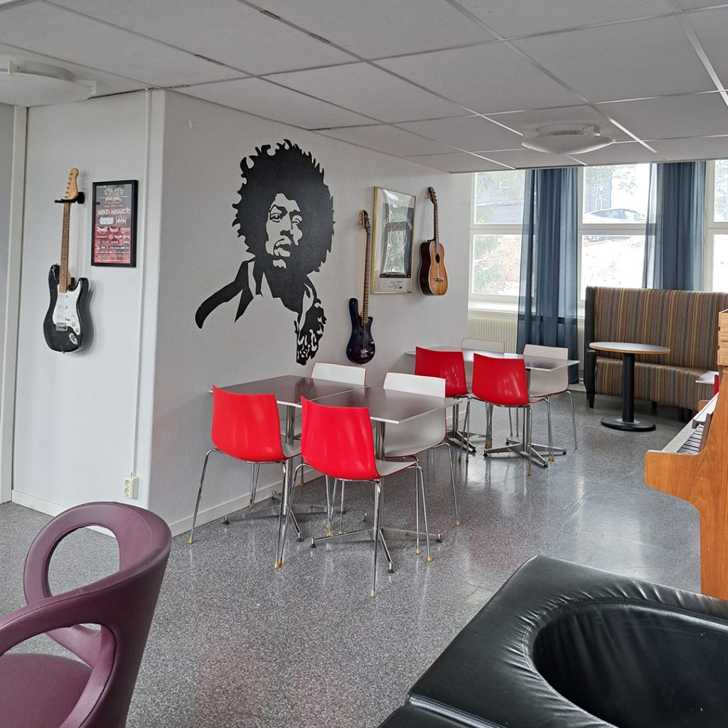 En lounge med röda stolar, väggkonst av Jimi Hendrix, gitarrer och stora fönster som släpper in naturligt ljus.