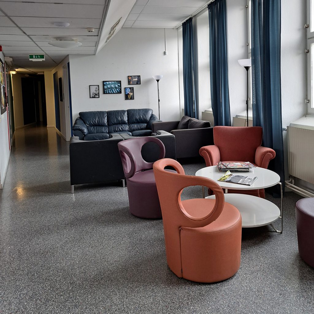 En lounge med moderna stolar, soffor, ett soffbord med tidskrifter och stora fönster med blå gardiner.