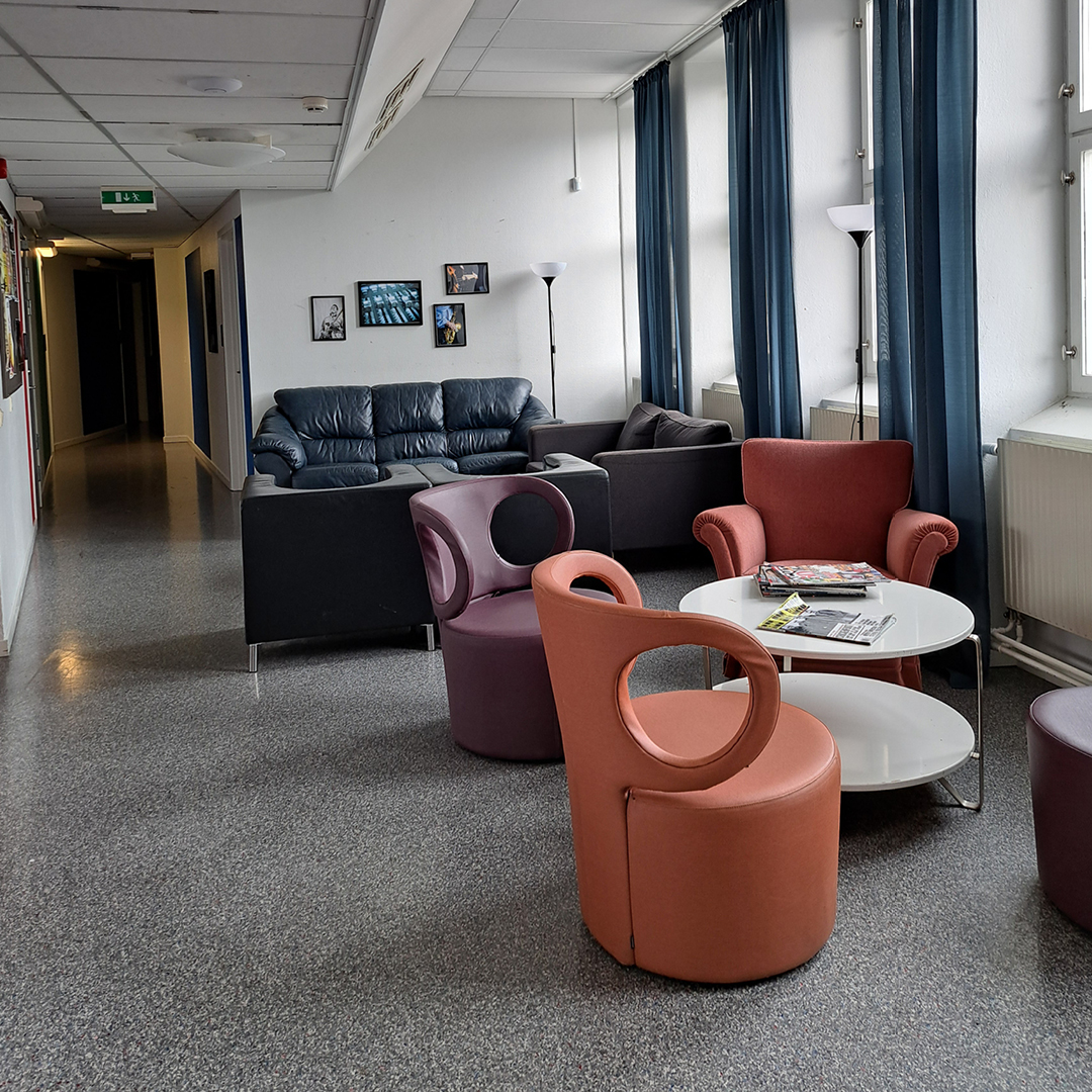 En lounge med moderna stolar, soffor, ett soffbord med tidskrifter och stora fönster med blå gardiner.