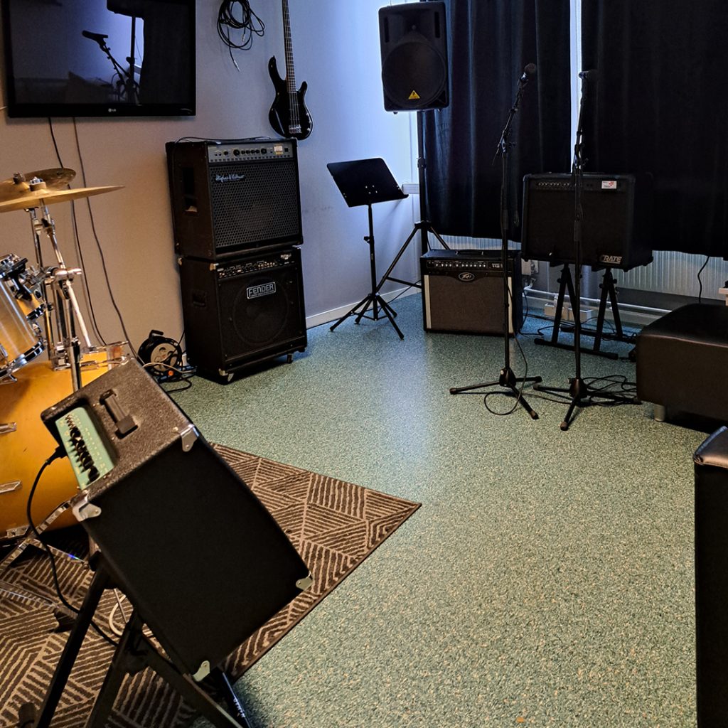 Musikrepetitionsrum med trumset, förstärkare, högtalare, mikrofonstativ och elgitarr.