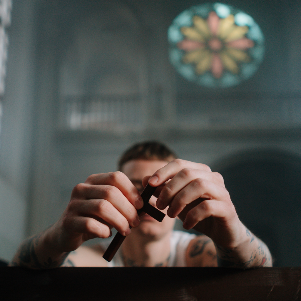 En kille som sitter i en kyrkbänk och håller i ett kors