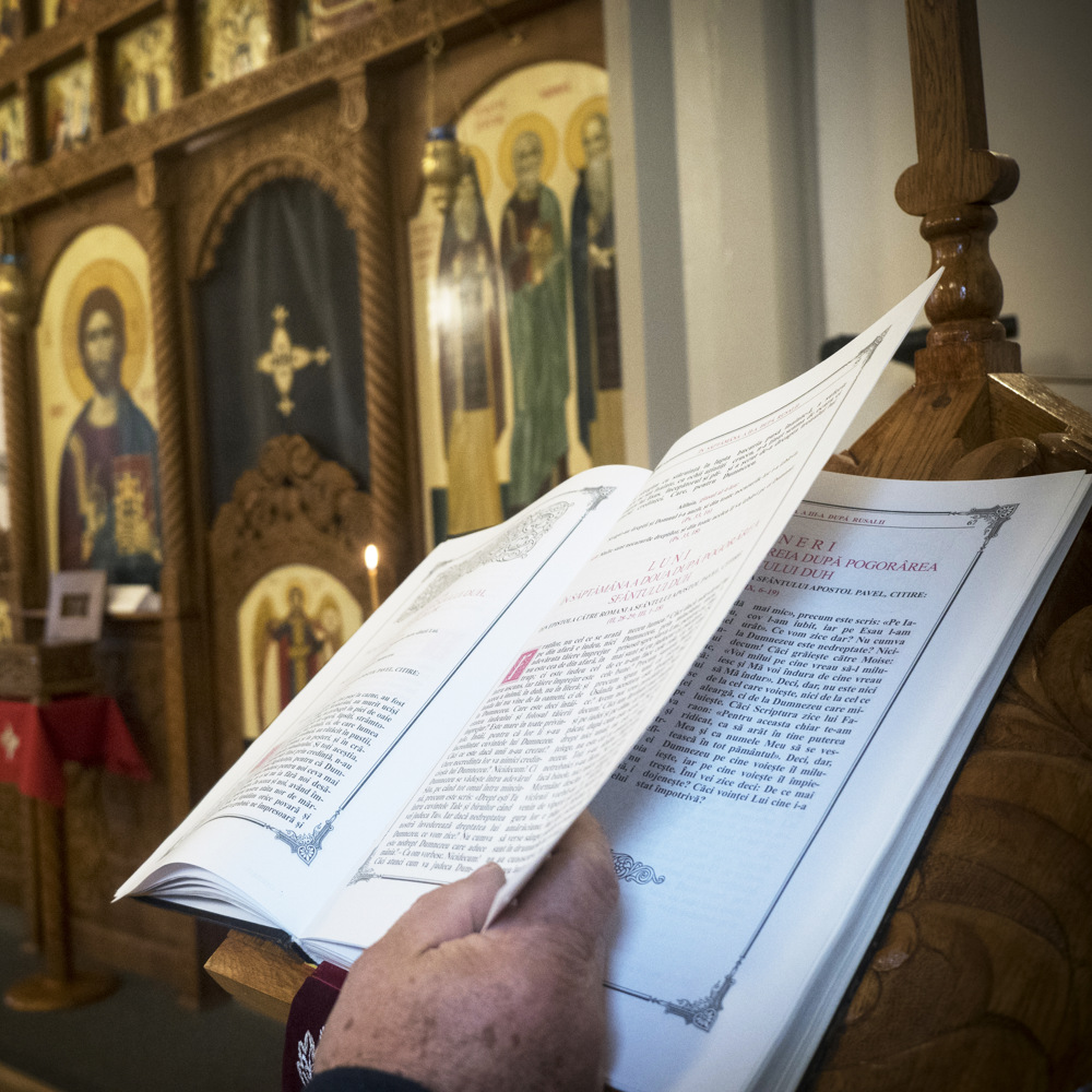 En person håller i en öppen bok framför utsmyckade religiösa ikoner i en ortodox kyrka.