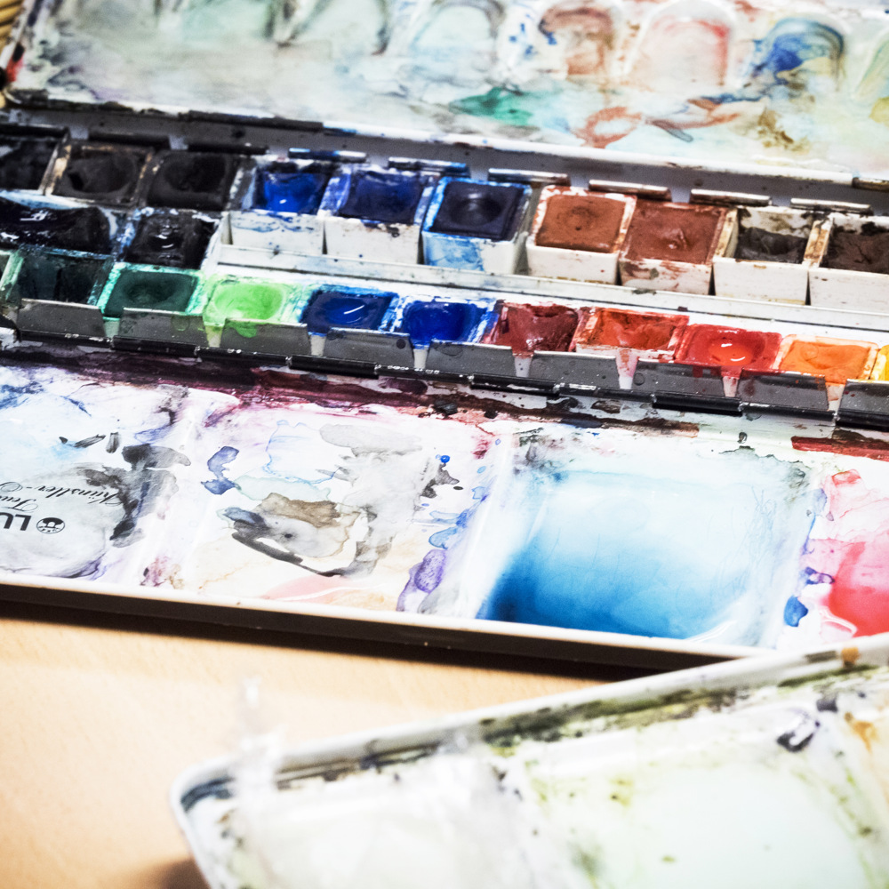 En öppen akvarellpalett med olika färgglada färger och blandningsytor på ett bord.
