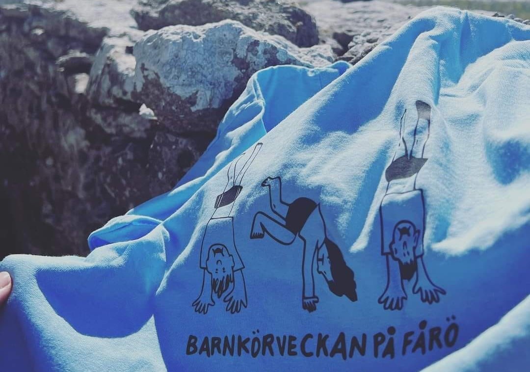 En blå tröja med tecknade barn som gör handstående och texten "BARNKÖRVECKAN PÅ FÅRÖ.