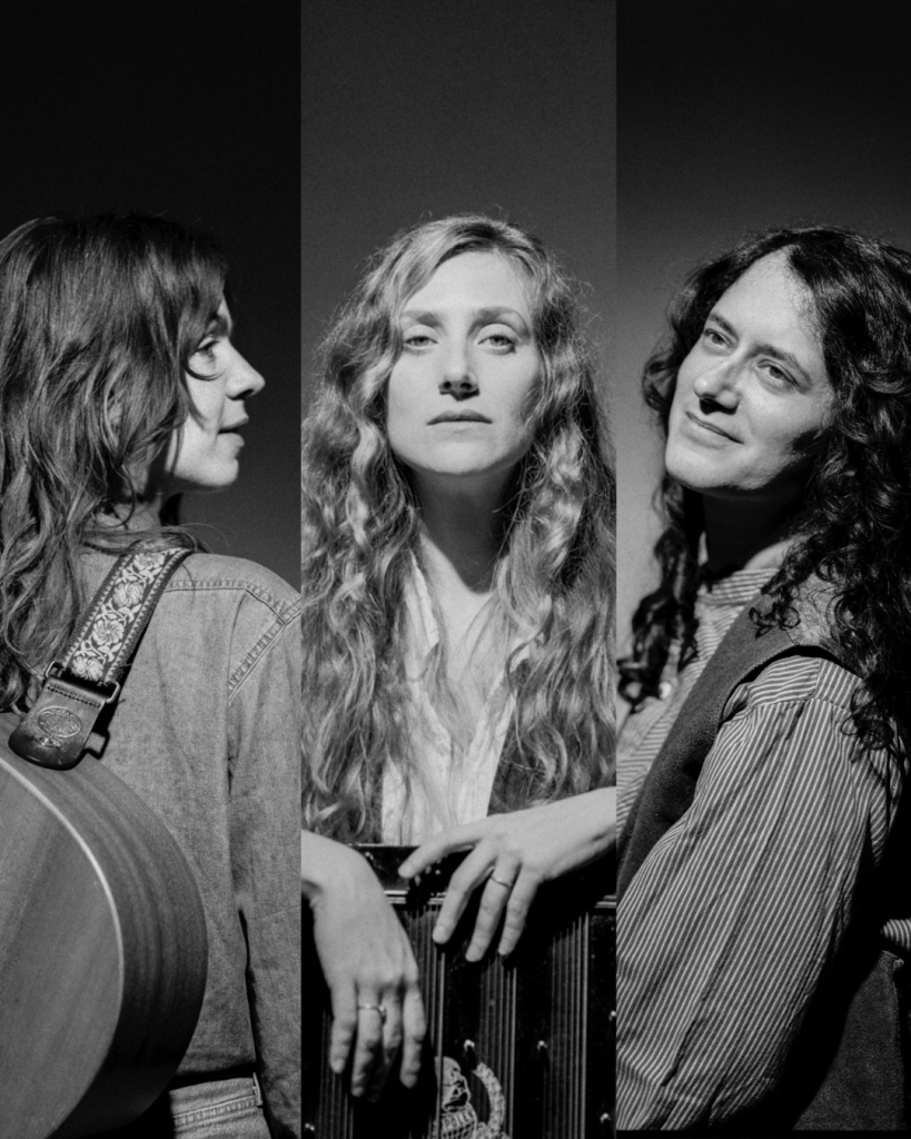 Svartvitt foto av tre kvinnor med långt hår, en håller i en gitarr, en annan håller i ett dragspel.