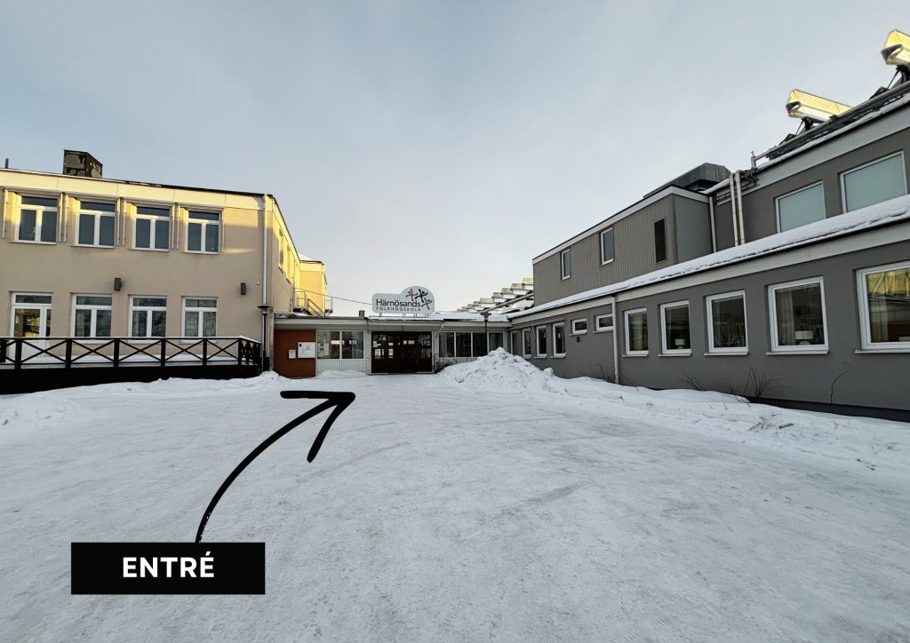 En snötäckt skolentré med en skylt, pil och textetikett "ENTRÉ" som pekar mot dörrarna.