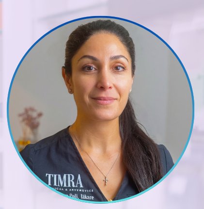 En kvinna i läkarrock med hästsvans och ett litet leende står i en klinisk miljö.