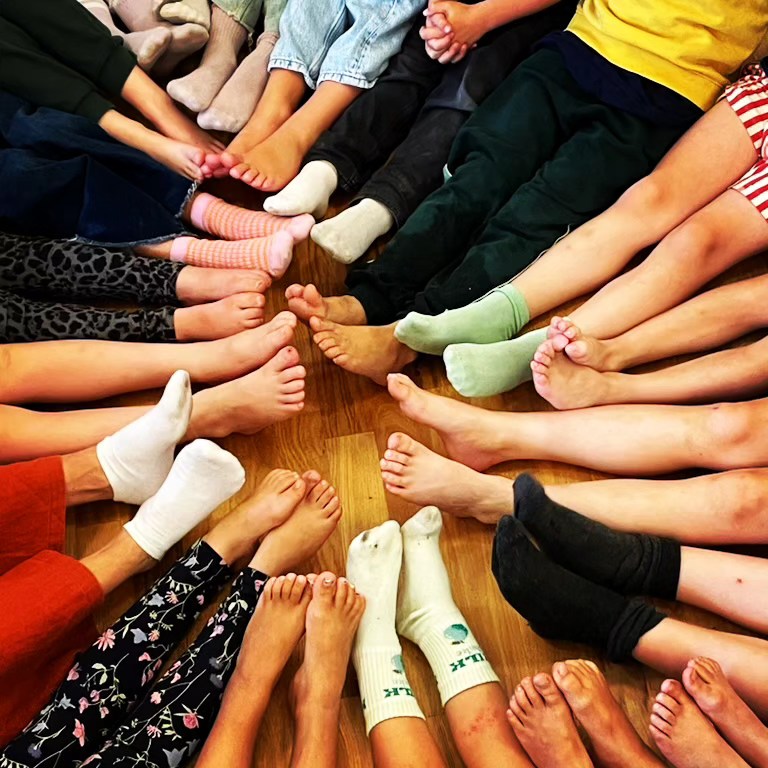 En grupp människor som sitter i en cirkel med fötterna utsträckta mot mitten, iklädda olika strumpor.