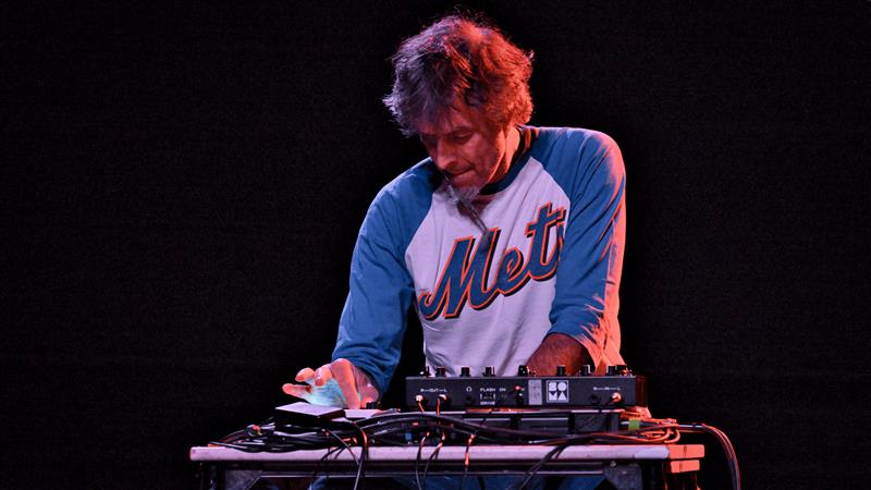 Man i Mets-skjorta sköter musikutrustning på en mörk scen.