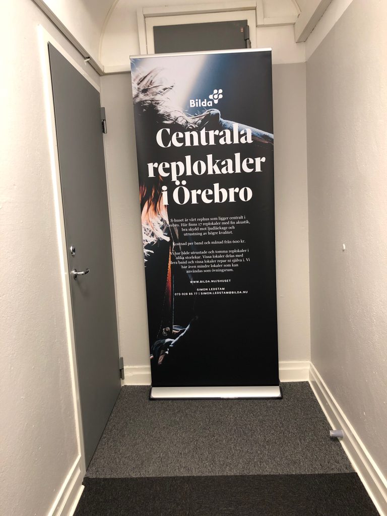 På en vertikal banner i en korridor står det "Centrala replokaler i Örebro" med grafik med musiktema.
