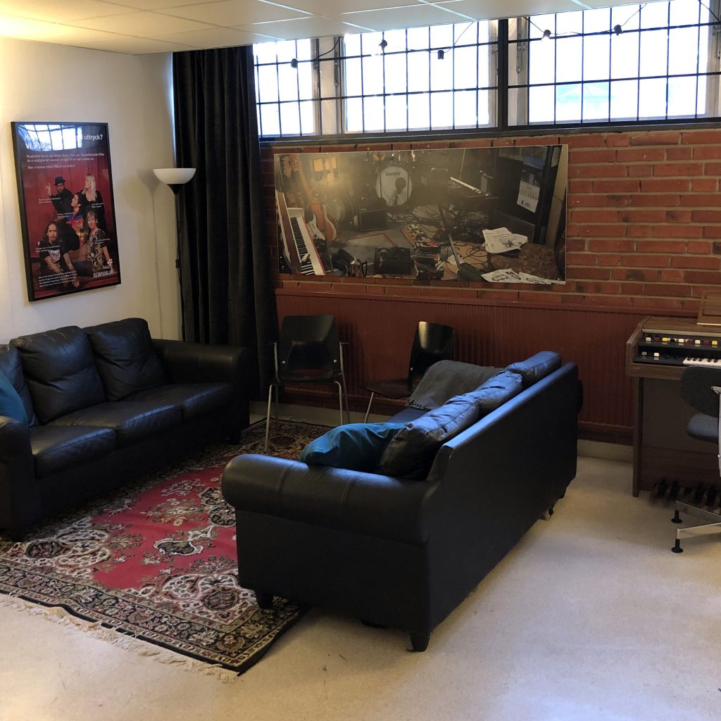 Två svarta soffor och en matta i ett mysigt rum med affischer på väggen och ett litet mixerbord.