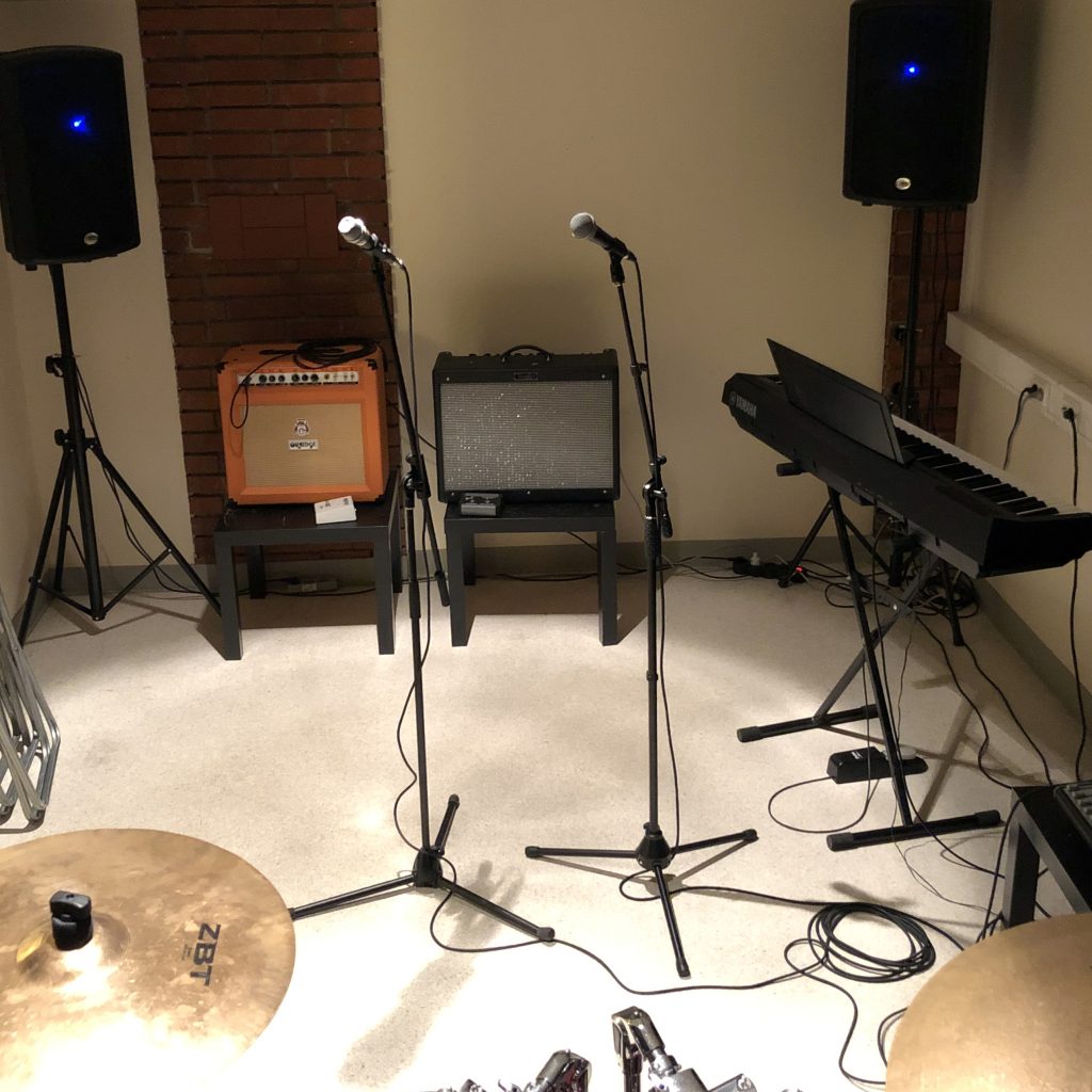 Ett musikrepetitionsrum med mikrofoner, högtalare, gitarrförstärkare, keyboard och trumcymbaler.