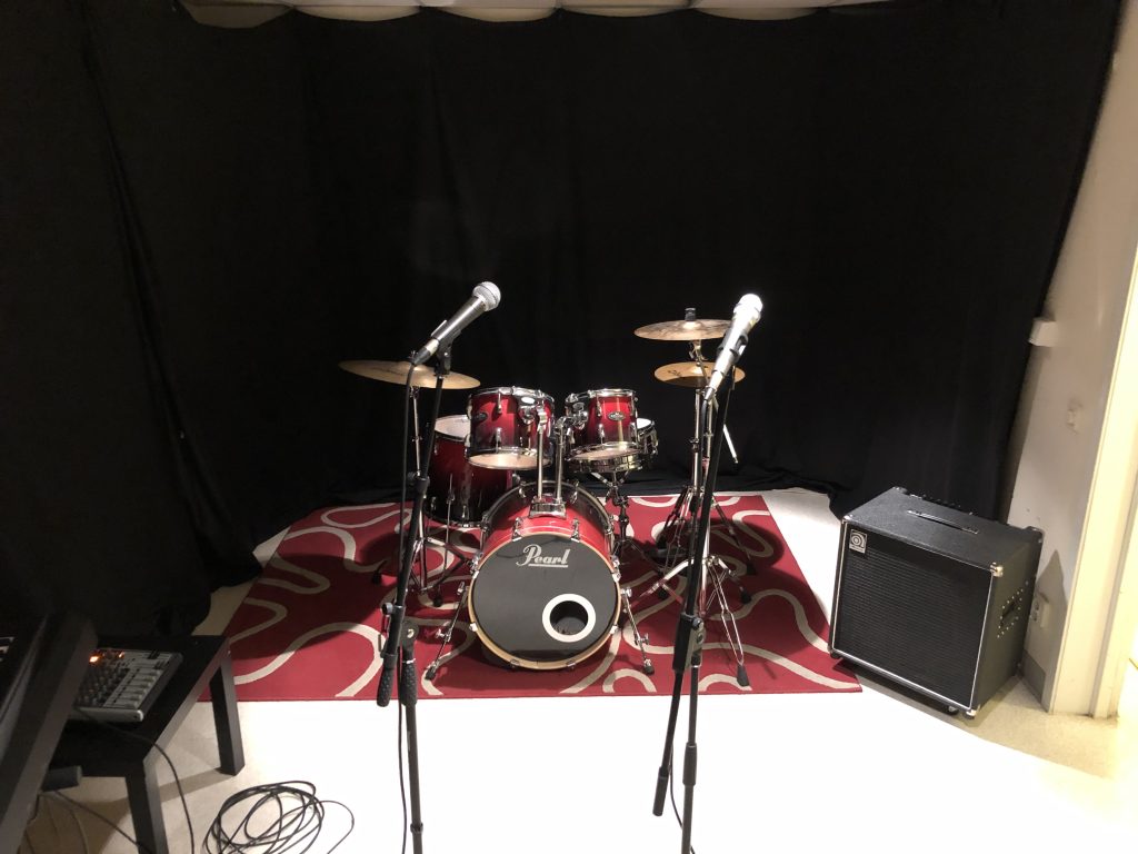 Ett rött trumset med två mikrofoner framför, på en röd matta med en svart bakgrund av gardiner.