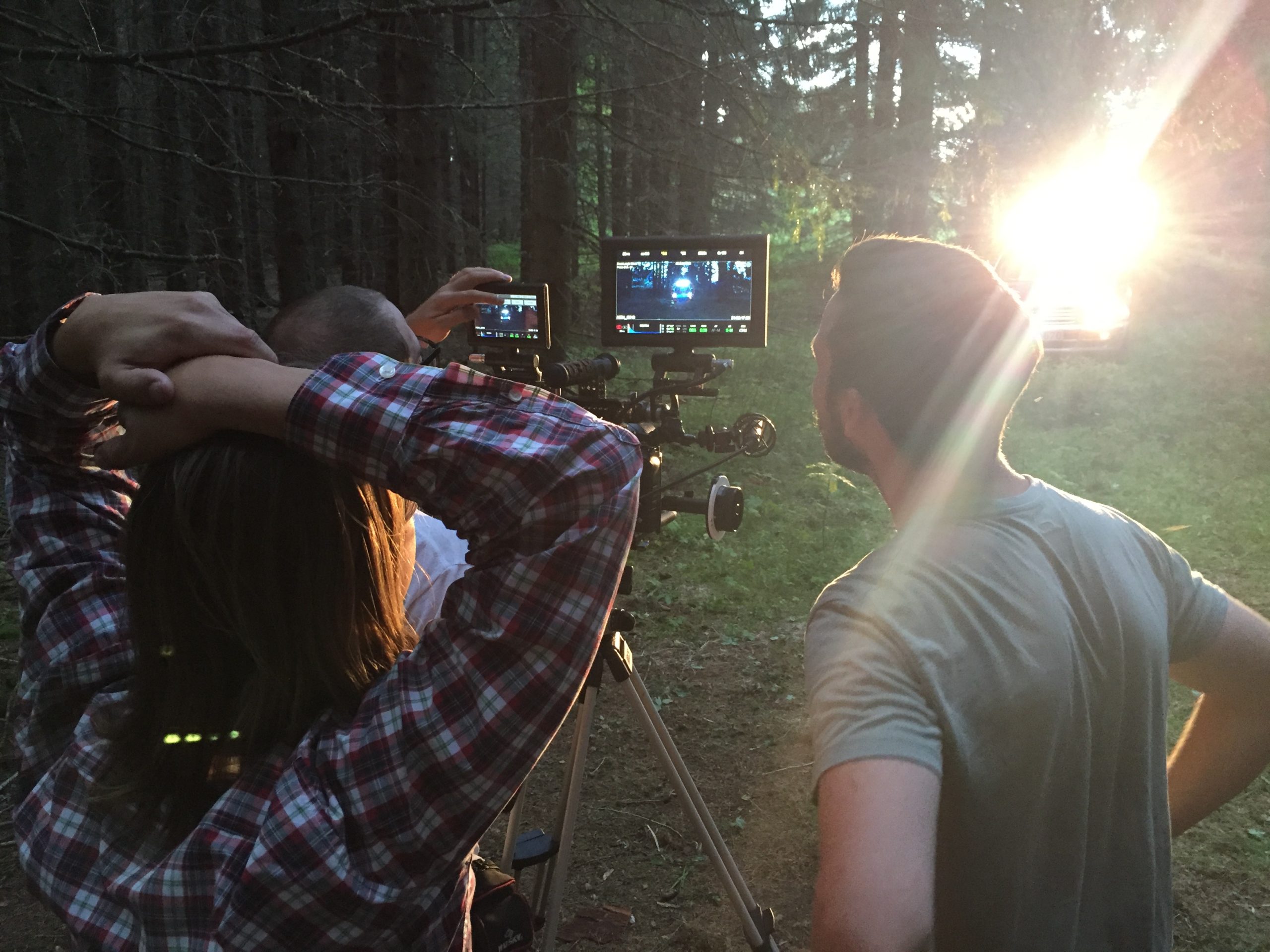 Två personer filmar en scen i en skog med hjälp av kameror och monitorer medan solljuset skiner genom träden.
