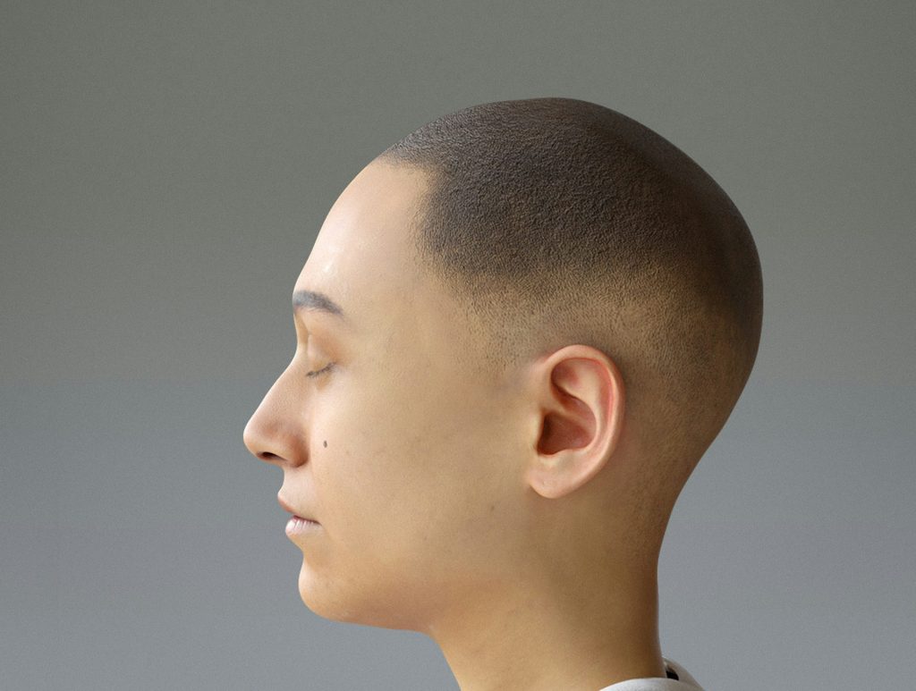 En person med rakat huvud i profil, med slutna ögon, mot en grå bakgrund.