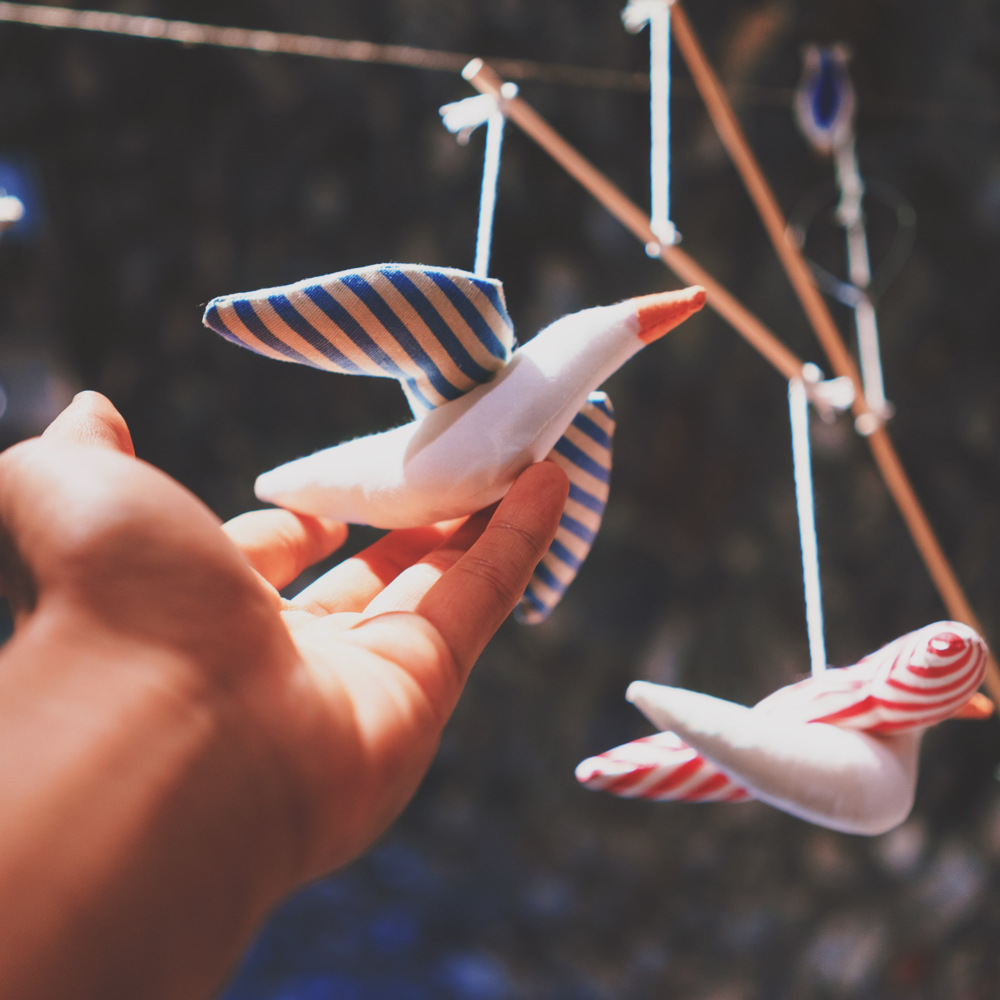 En hand sträcker sig mot en hängande fågelprydnad i tyg med blå och vita ränder.