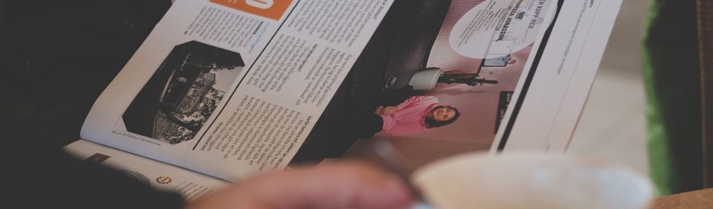 Person läser en tidning och håller i en vit kopp; en kvinna i rosa är avbildad i tidningen.