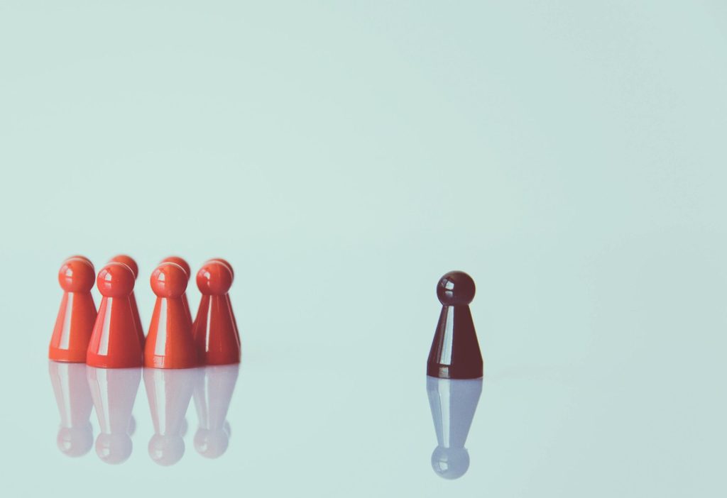 Fem röda spelpjäser grupperade tillsammans, med en mörkröd pjäs som står ensam till höger mot en ljus bakgrund.