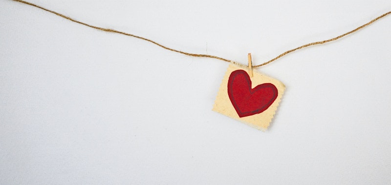 Ett rött hjärta på papper fäst i ett snöre mot en vit bakgrund.