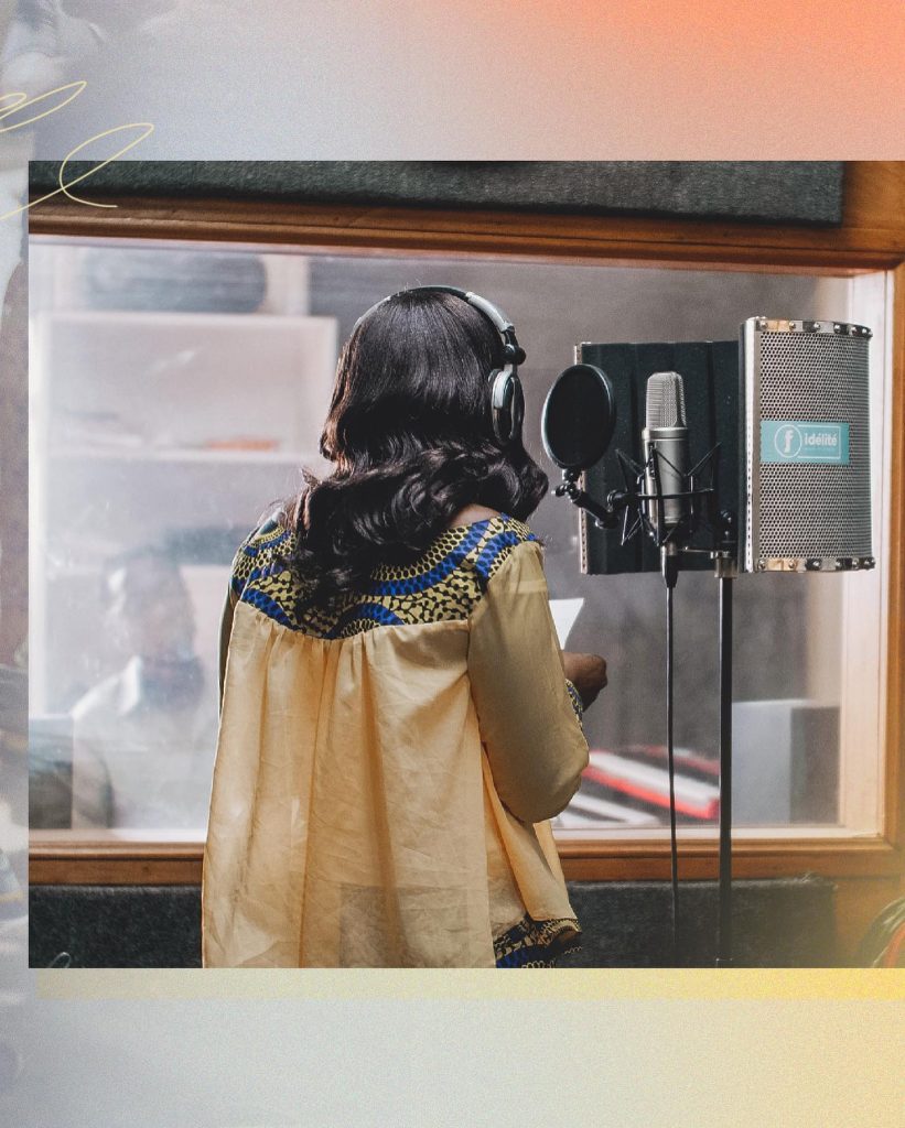 En mörkhårig kvinna med hörlurar står framför en mikrofon i en inspelningsstudio.