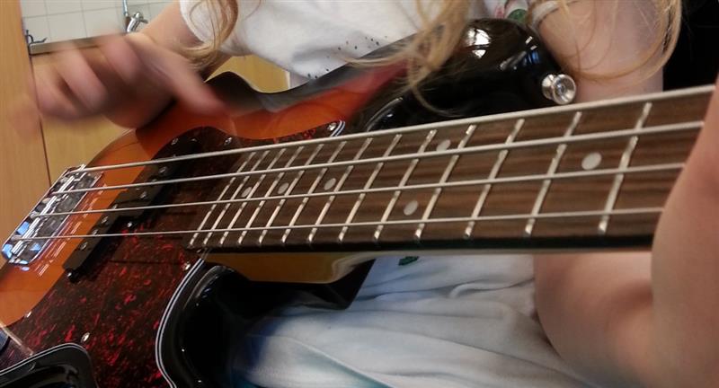 Närbild på en person som spelar en fyrsträngad elbasgitarr, med fokus på händerna och instrumentet.