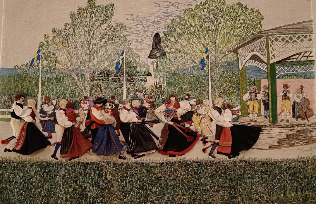 Människor i traditionella svenska kläder dansar utomhus nära musiker och svenska flaggor en solig dag.