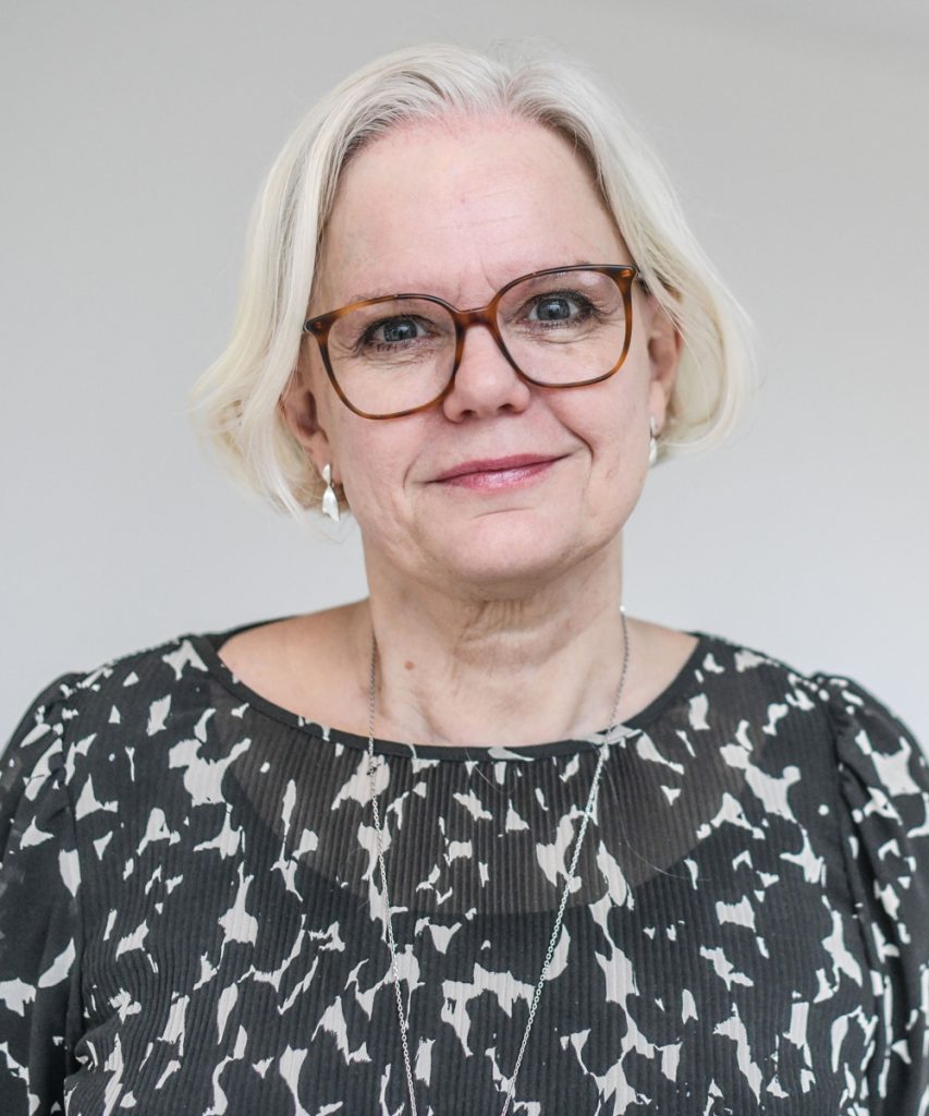 En kvinna med glasögon står i ett rum.