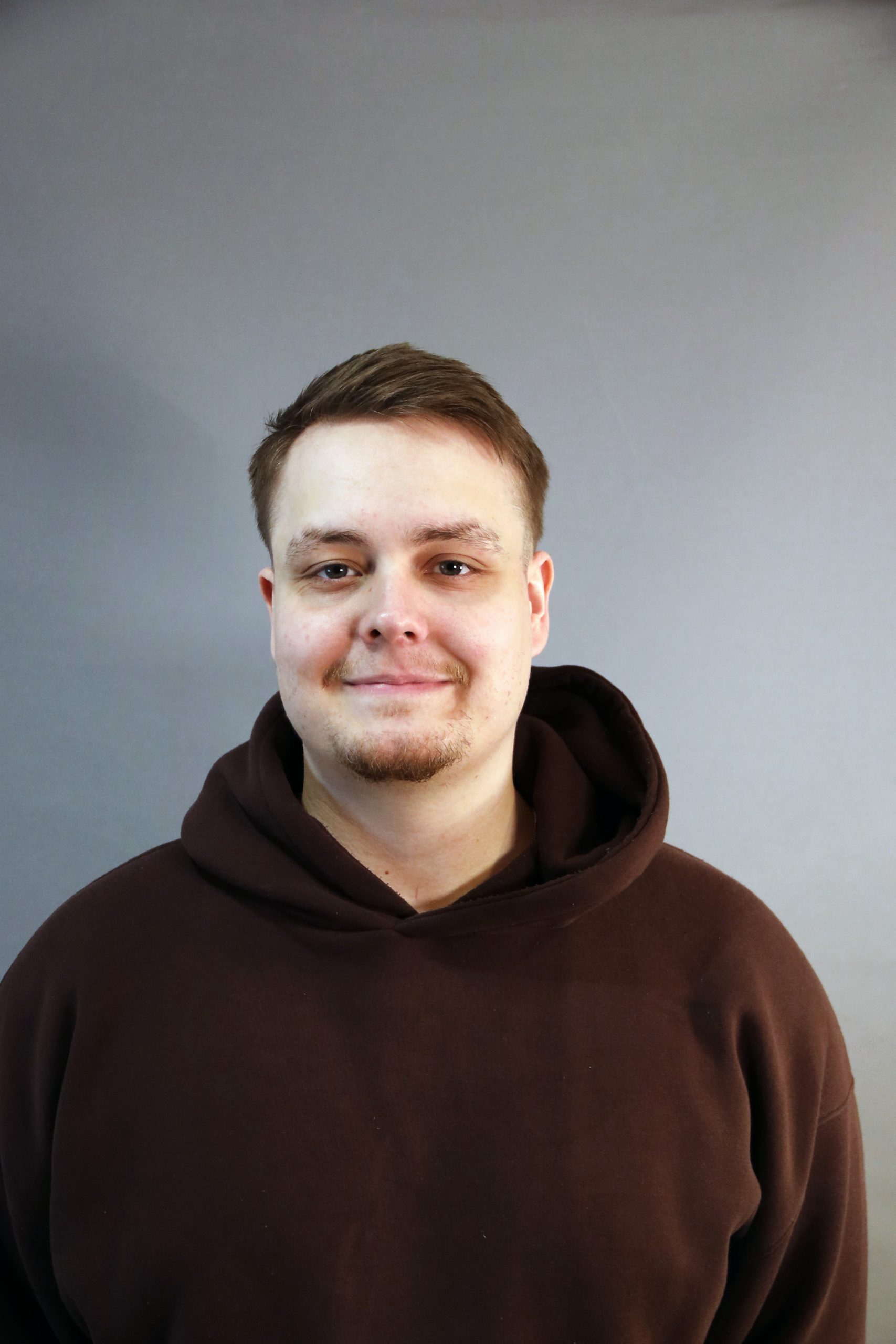 En person i brun huvtröja ler mot en grå bakgrund.
