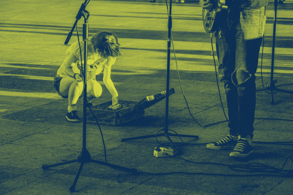 En person knäböjer för att lägga pengar i ett öppet gitarrfodral under ett gatumusikframträdande.