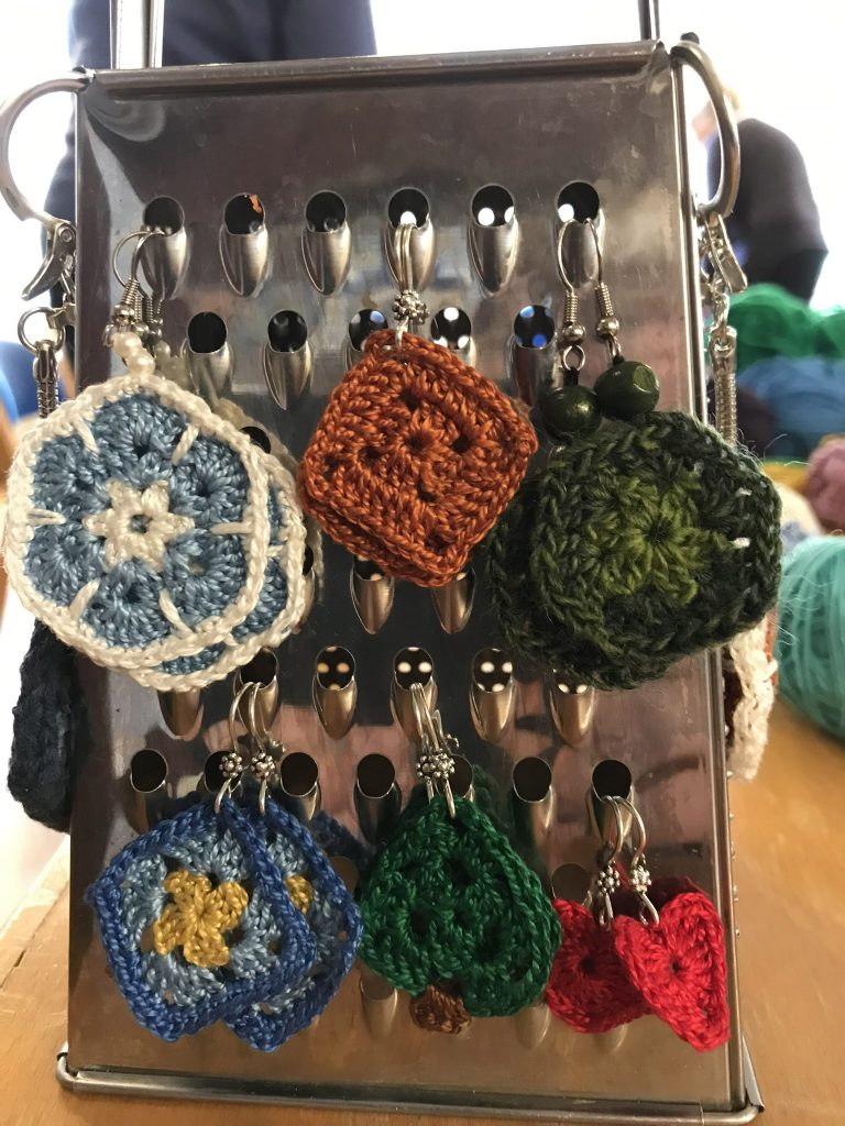 Färgglada virkade örhängen hängande på ett ostgaller i metall, använt som ett kreativt displayställ.