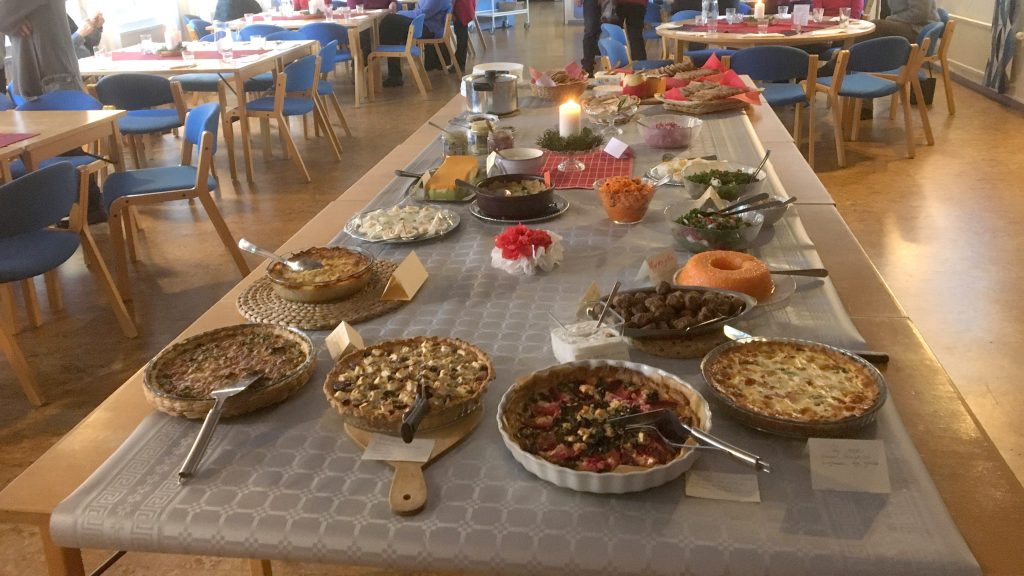 Ett långbord dukat med olika pajer, sallader och rätter i en ljus matsal med blå stolar.