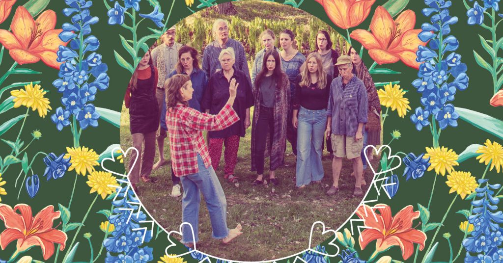 En barfota person leder en grupp som sjunger utomhus, omgiven av en färgglad blomsterrabatt.