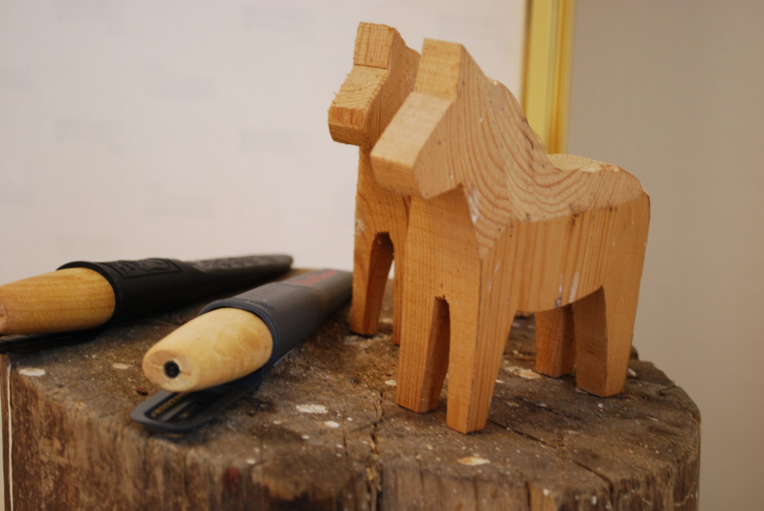 Två trähästar på en trästubbe. Bredvid ligger två täljknivar. 