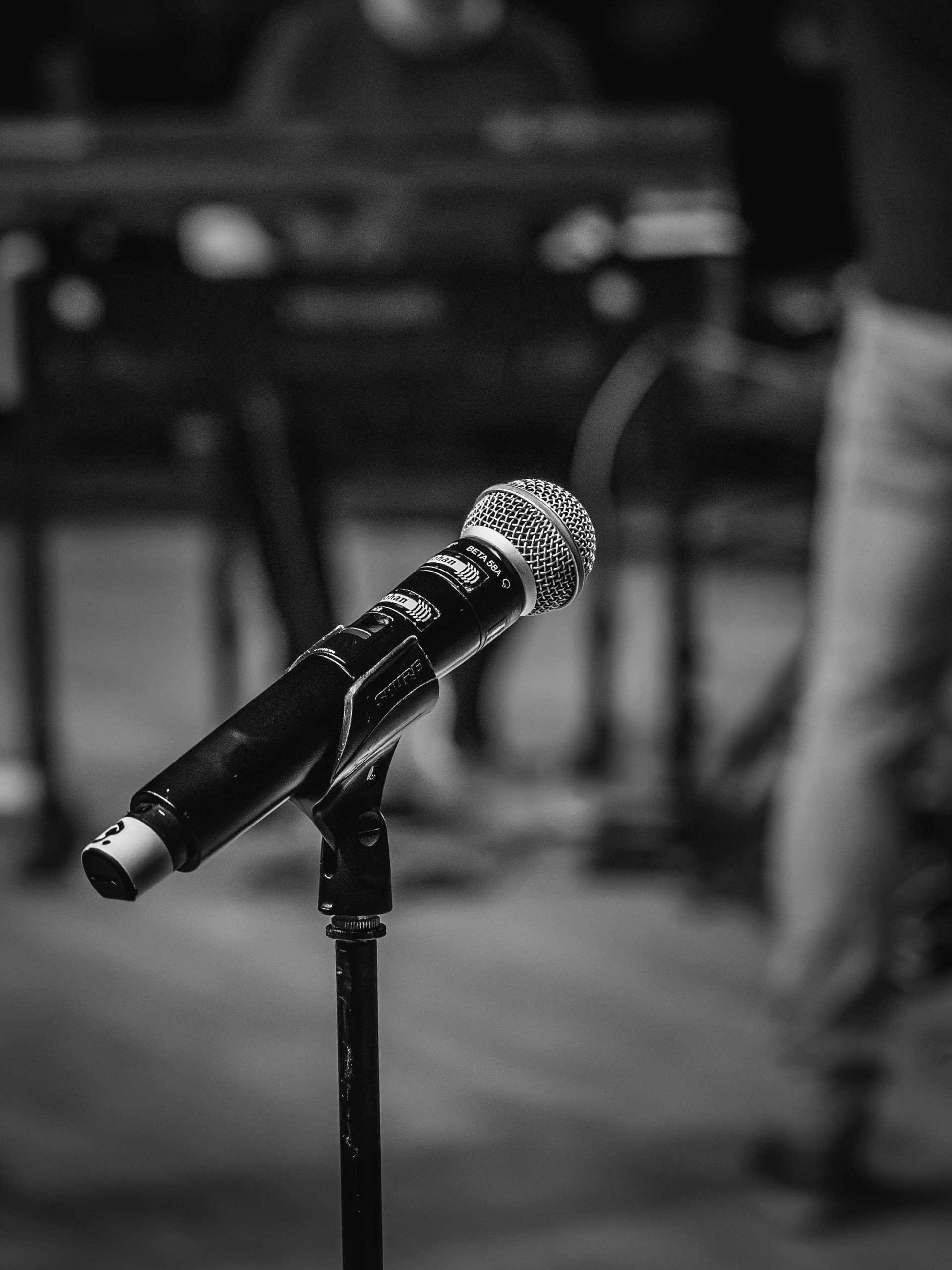 En mikrofon på ett stativ i fokus, med en oskarp bakgrund av musikutrustning och en person.
