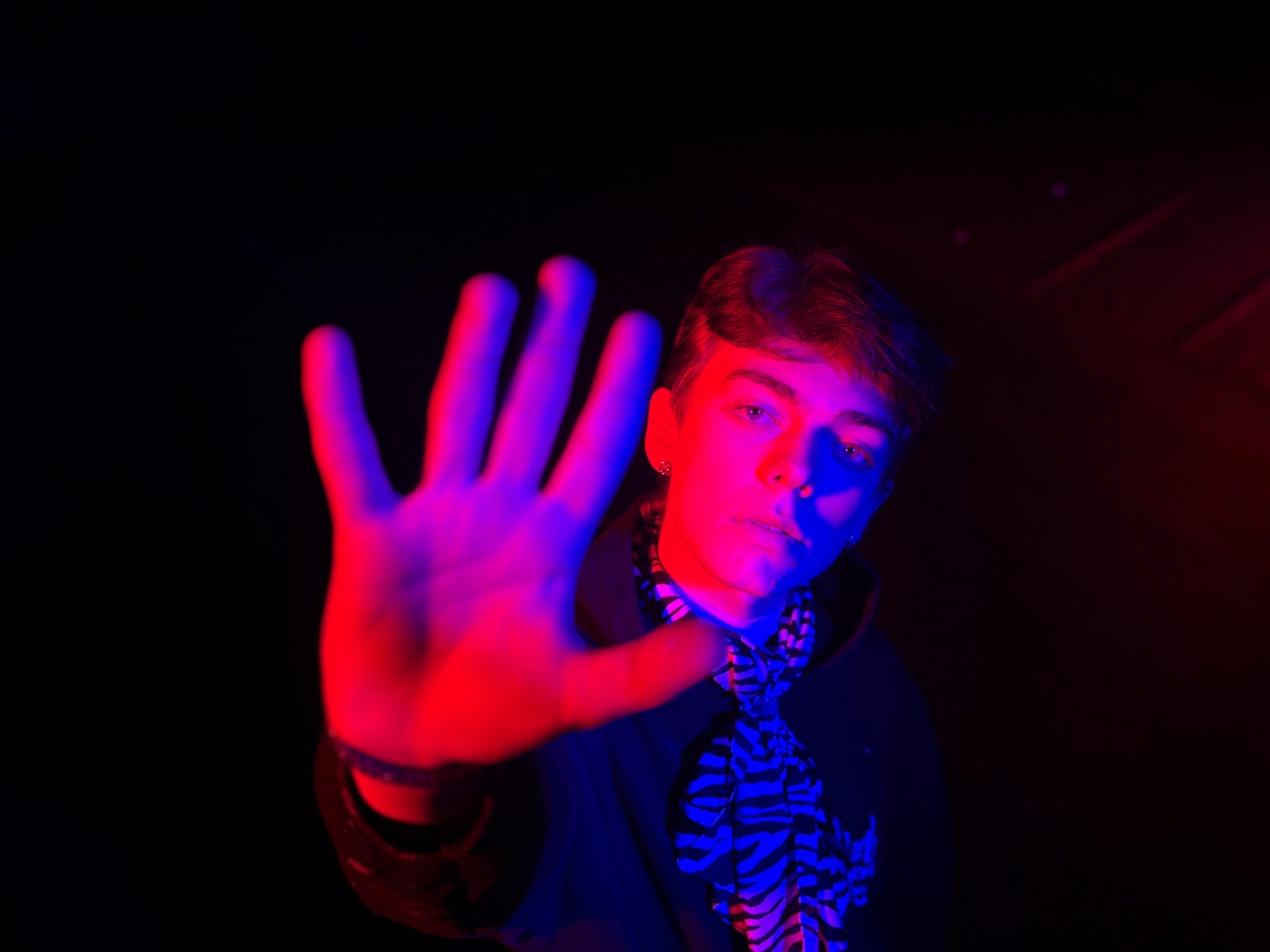 En person håller handen mot kameran, upplyst av röd och blå belysning mot en mörk bakgrund.