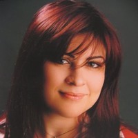 Leende kvinna med rakt rödbrunt hår och sidensvängd lugg mot en mörk bakgrund.