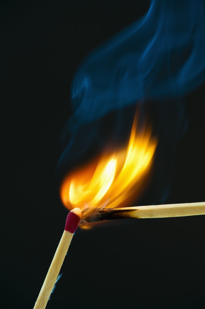 Två tändstickor mot en mörk bakgrund, den ena tänder den andra med en ljus låga och virvlande rök.