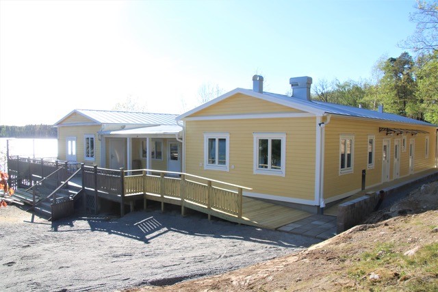 Gula träbyggnader med vita lister, ramper och räcken, belägna nära ett vattendrag och träd.