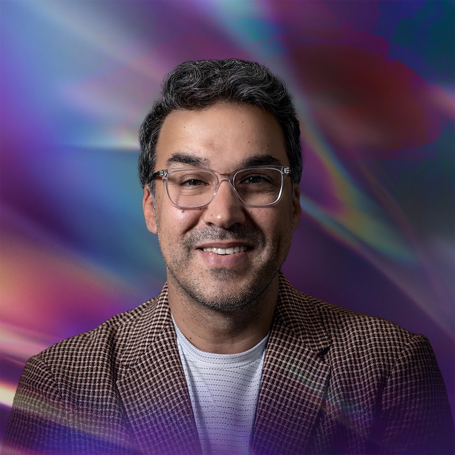 Man med glasögon och rutig kavaj ler med en färgstark, abstrakt bakgrund bakom sig.