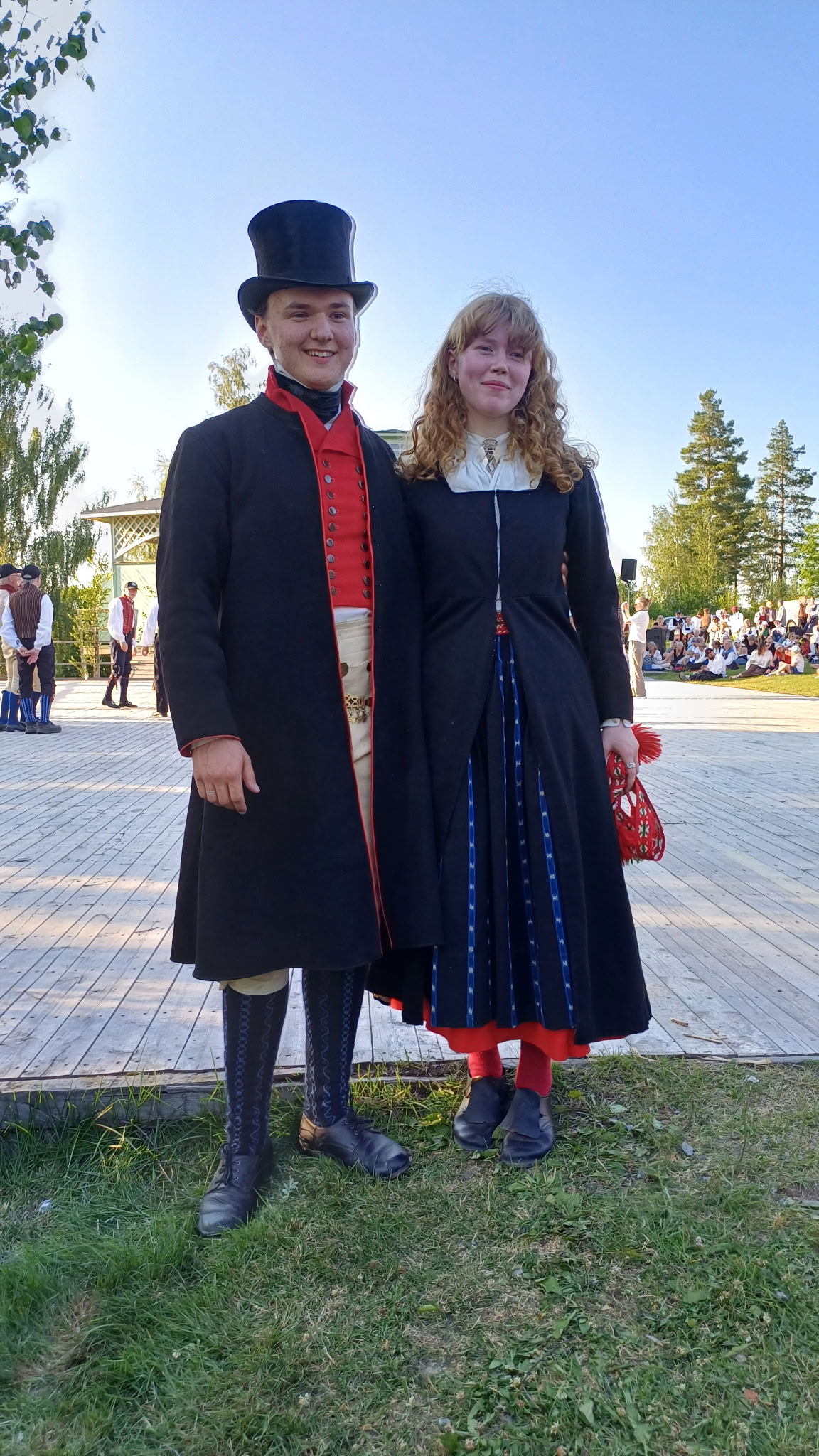 En man och en kvinna i traditionella nordiska folkdräkter står utomhus en solig dag.
