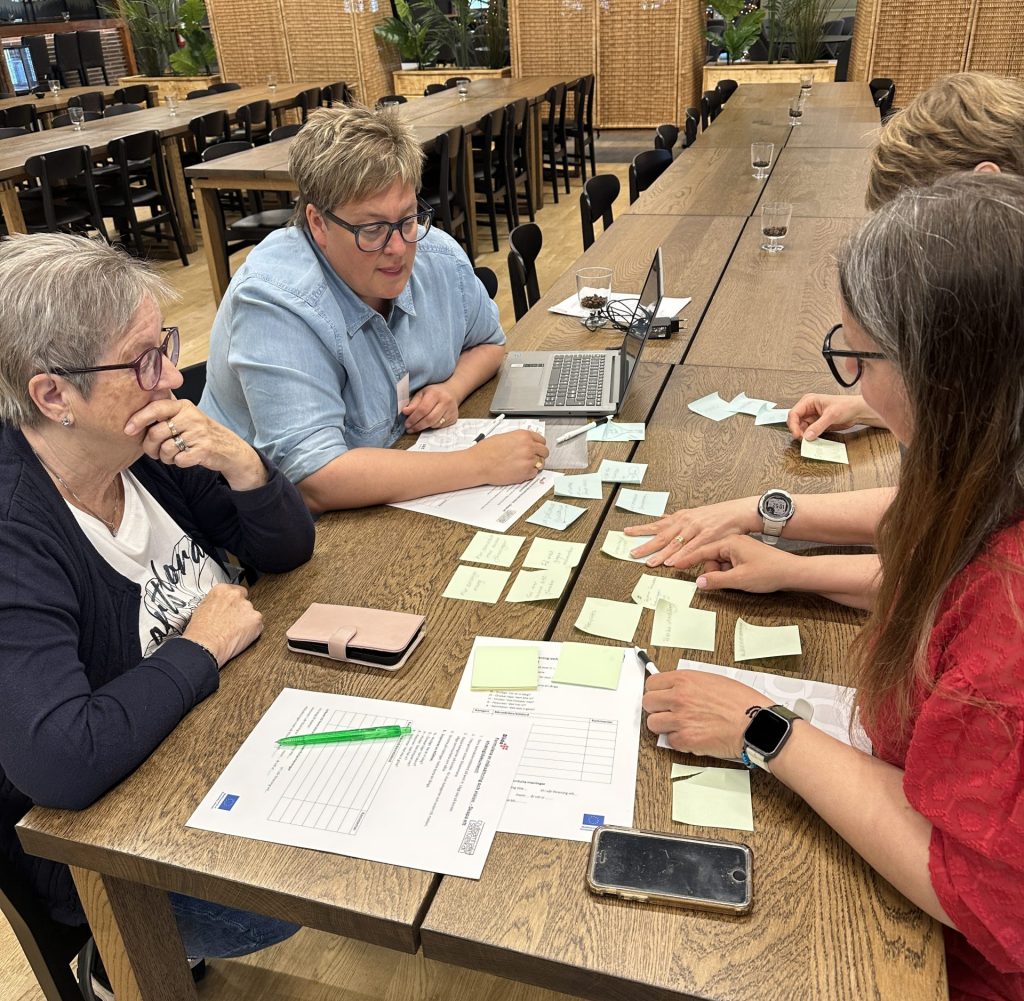 Fyra personer sitter vid ett långbord och diskuterar och sorterar klisterlappar under en gemensam workshop.