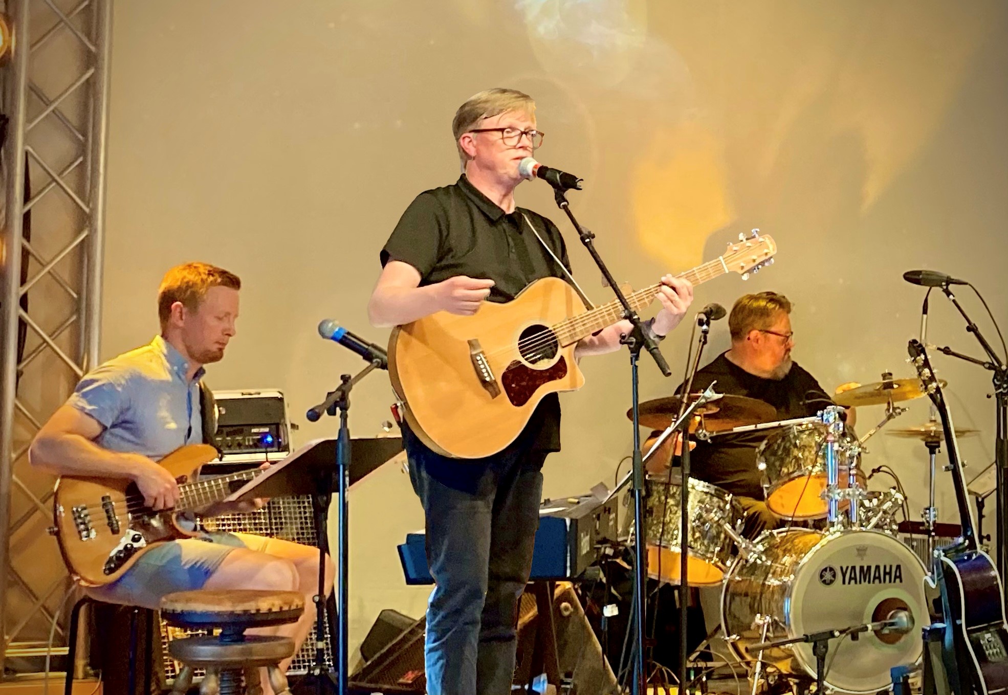 Ett tremannaband spelar på scenen med gitarr, bas och trummor under varm scenbelysning.