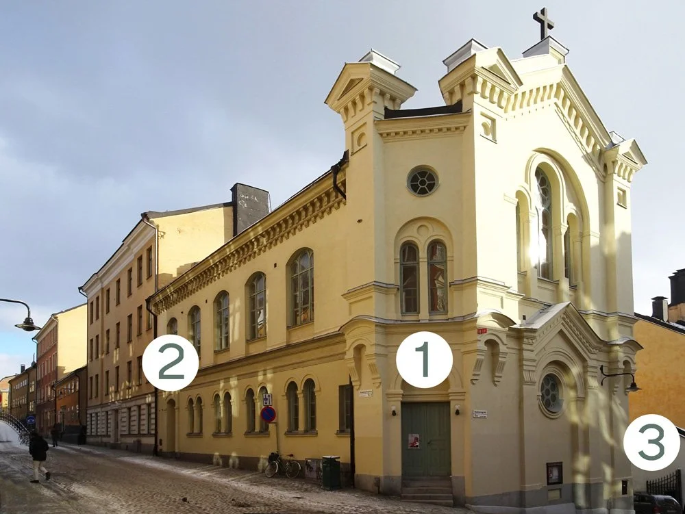 En ljusgul kyrkobyggnad på en kullerstensgata, med siffrorna 1, 2 och 3 som markerar delar av fasaden.