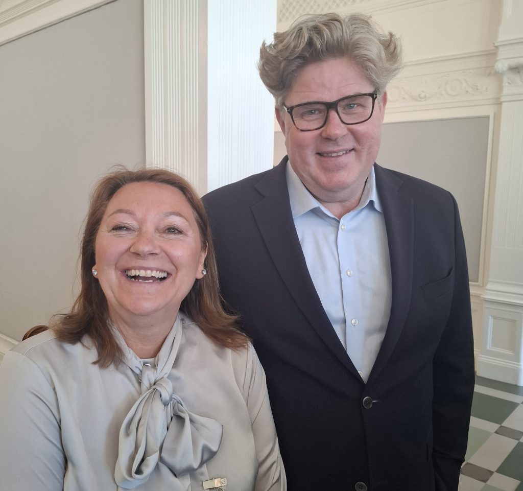 Jeanette Borssén och Gunnar Strömmer ler och står tillsammans i ett ljust, elegant rum med vita väggar.