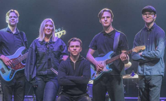 Fem musiker poserar på scenen med gitarrer, bas och trummor, i blå-lila scenbelysning.